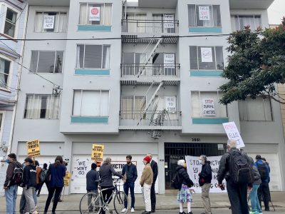 a group of people with signs picket an apartment building