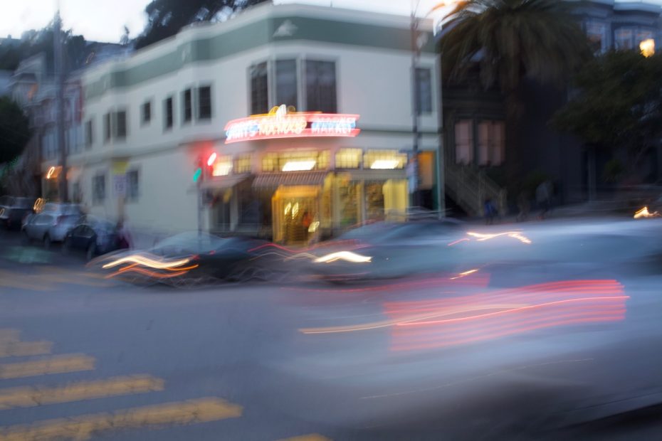 A blurry image of Mama's Market on Dolores Street at dusk, with headlights streaming by.