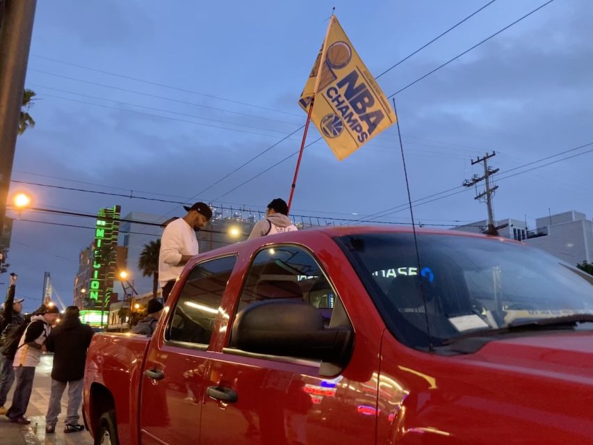 A Warriors NBA Champs flag waves out of a pickup truck.