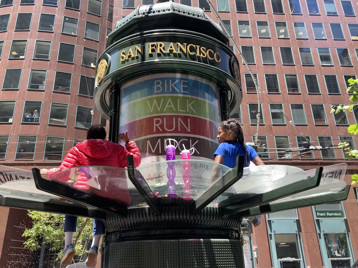 Two young girls perch above the crowd on a newsstand.