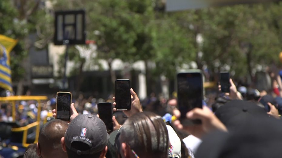 Fans in the crowd film the parade with their phones.