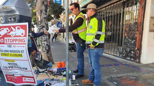 Public Works staffers hand a woman a flyer about how to obtain a permit to sell merchandise