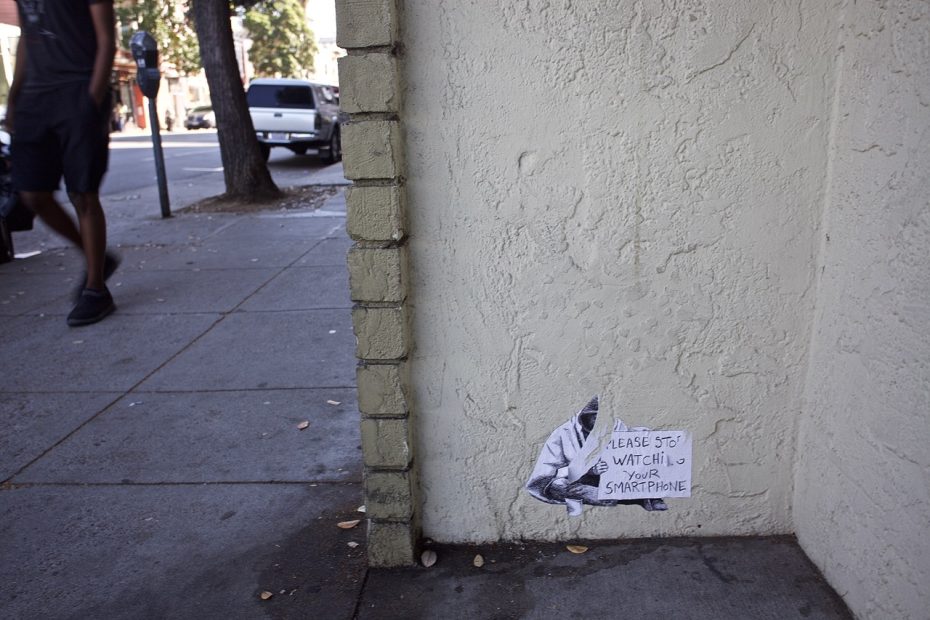 Small stencil on a corner wall telling people to get off their cell phones.