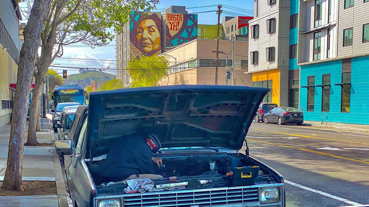 A car with its hood open and a mural in the background.