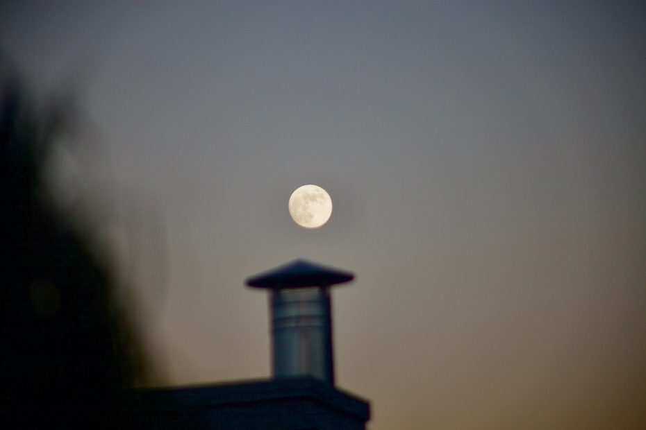 The full moon rising over a steeple.