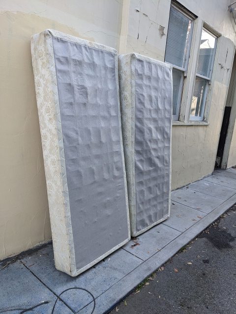 Two box springs up against an outside wall.