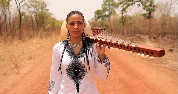 A woman on a dirt road with an instrument over her shoulder.
