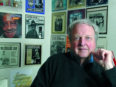 A man with a wall of record labels behind him.