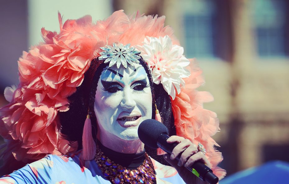 A drag queen with a colorful headdress and a microphone.