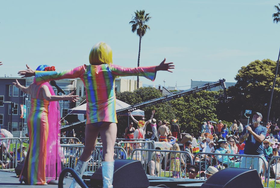 Someone in a rainbow minidress with their hands stretched. And a palm tree in the background.