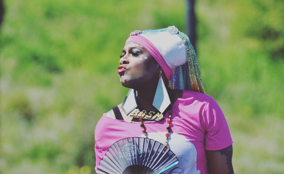 A person with a beaded headdress, large kite-shaped earrings and a fan.
