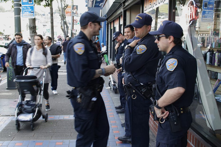 Five officers standing around and a woman with a baby stroller walking toward us. 