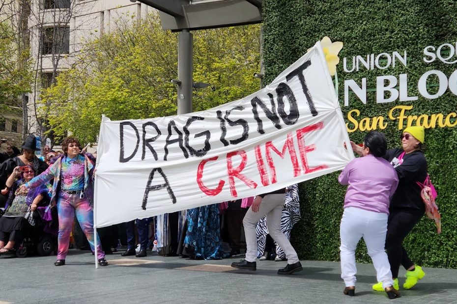 Drag kings Luke Modelo and Jota Mercury hold a banner saying, drag is not a crime.