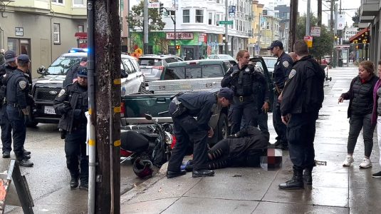 A Black woman handcuffed on the ground and surrounded by several San Francisco police officers.