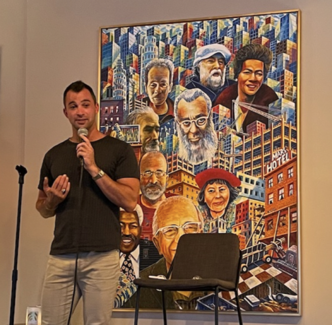 Manny Yekutiel holding a microphone and speaking.