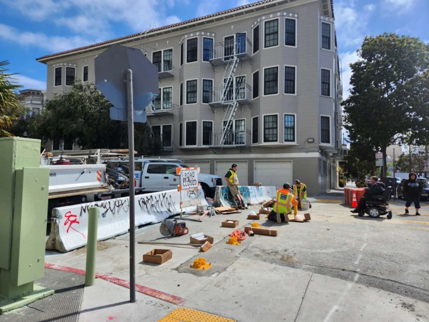 work crew standing around steel bollards being installed on the street
