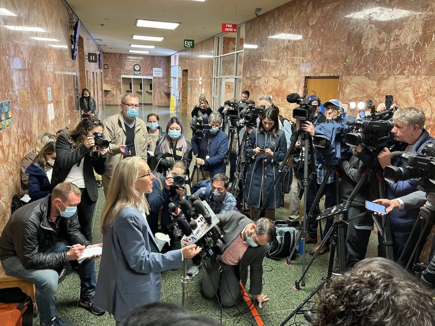 A woman addresses a few dozen members of the press
