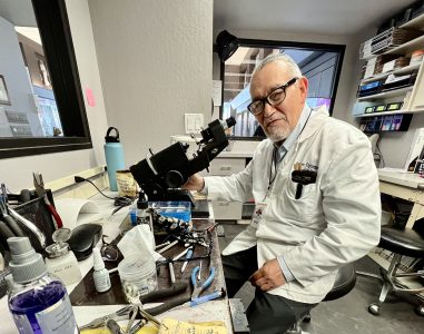 A man in a white lab coat sitting at a table with glasses.