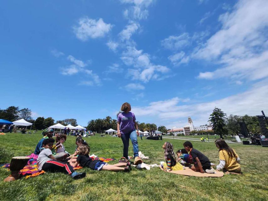 An adult and some kids on the ground in a park before the Trans March