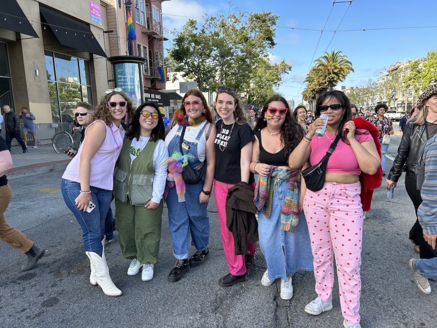 Six young women, wearing various bright colors, pose together during a lesbian pride march.