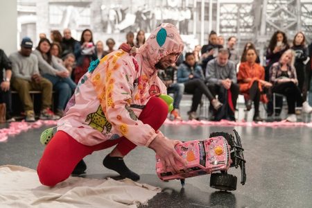 A man in a pink costume kneeling on the floor in front of a crowd.