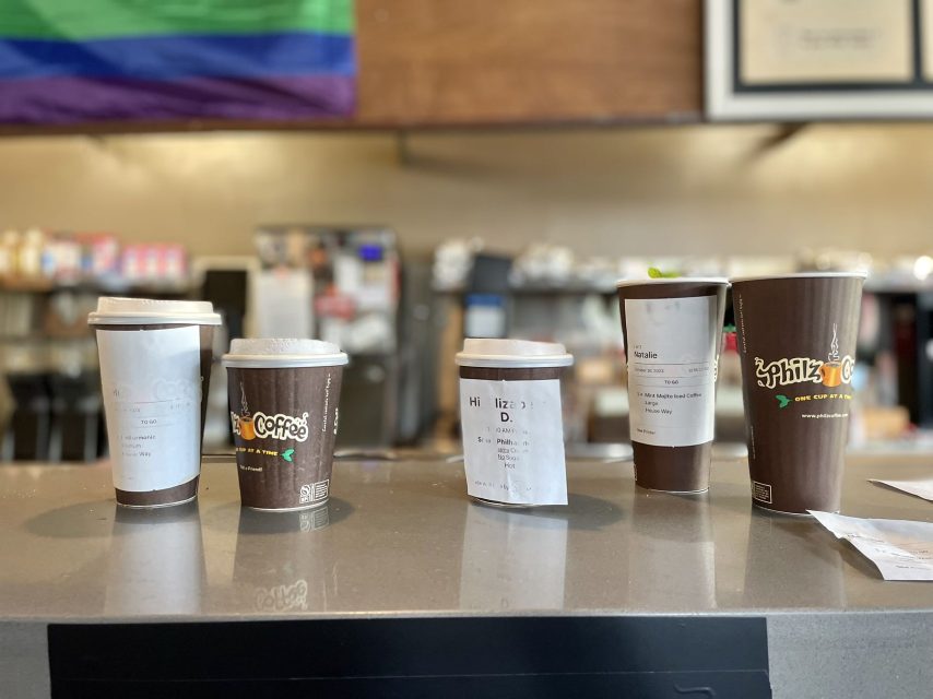 A line of Philz coffee cups on a counter with an lgbt flag.
