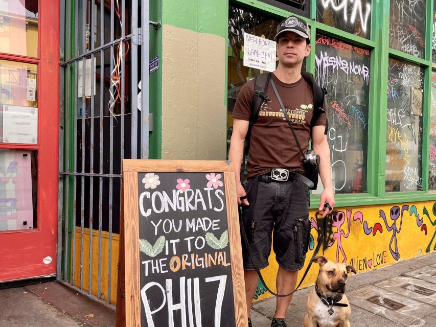 A man with a dog standing in front of a Philz sign.