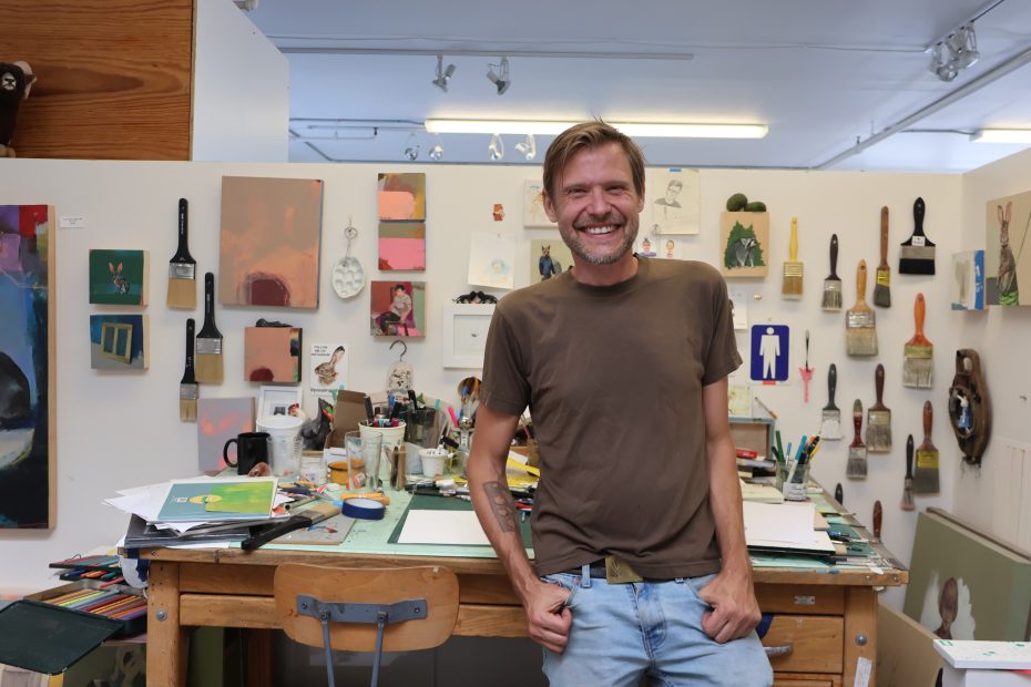 A man standing in front of a desk covered in paper and tools.