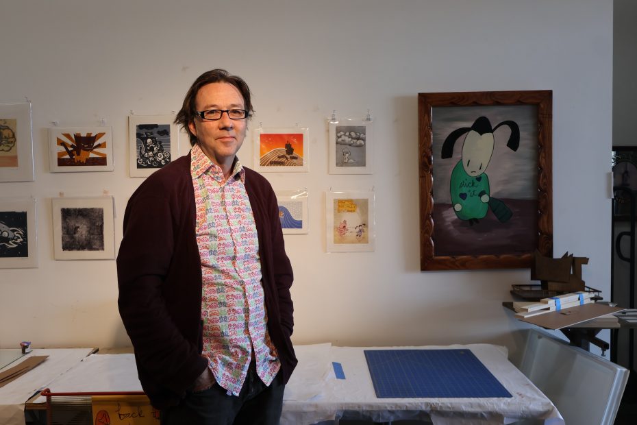 A man standing in front of a wall with artworks. 