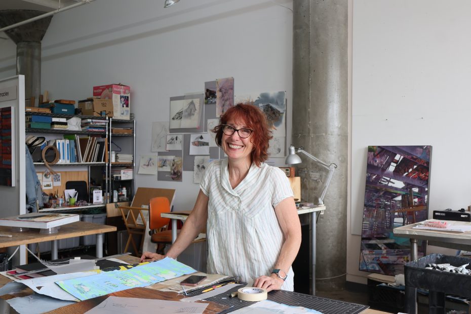 A woman standing in front of a desk with a lot of papers.