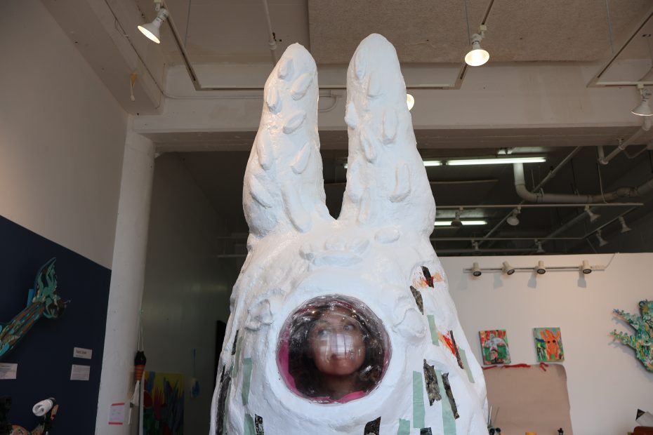 A sculpture of a rabbit with a round window and a person smiling through it.