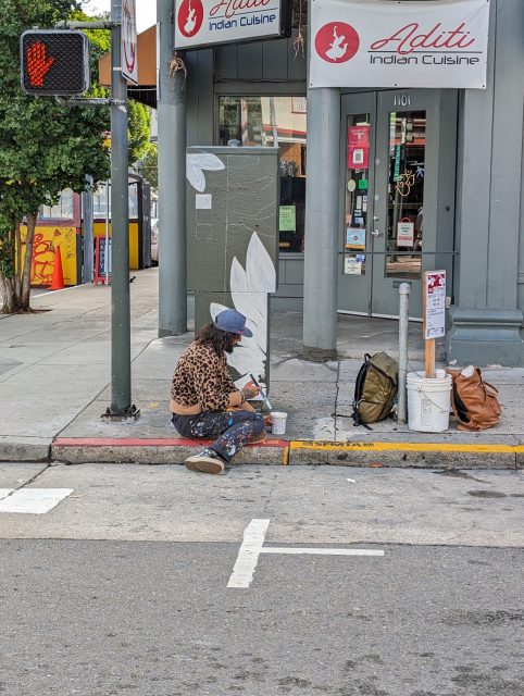 A person painting petals on an electricity cabinet.