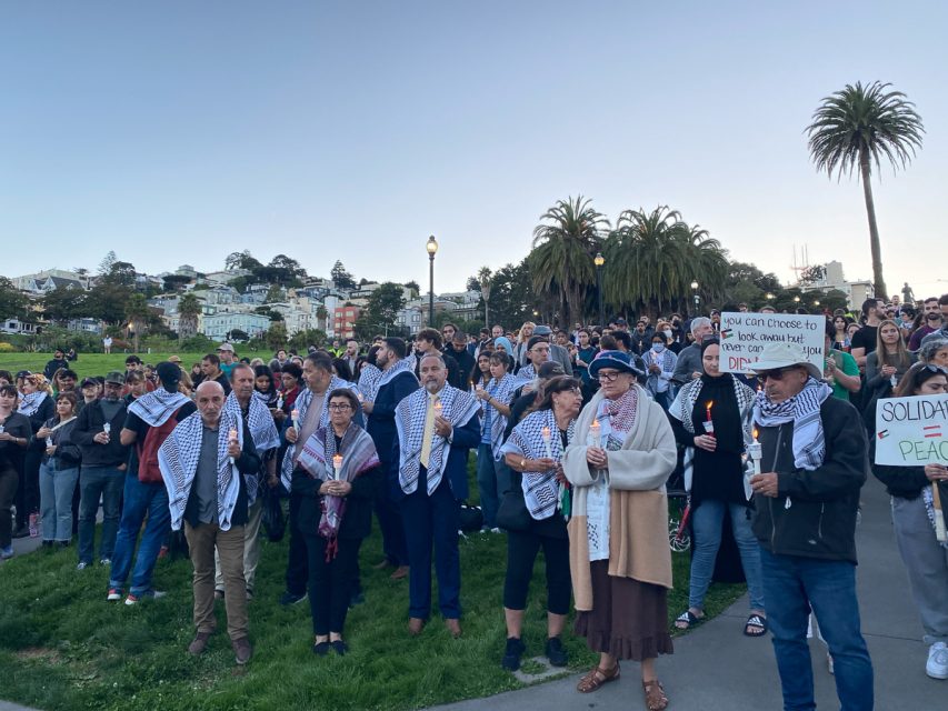 A group of people holding signs and candles in a park.