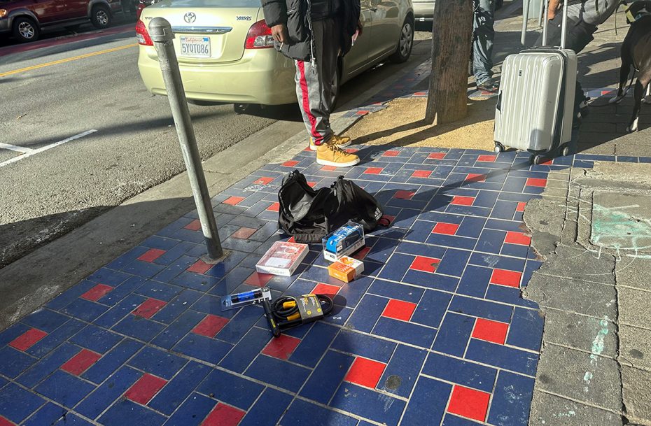 A man standing on a sidewalk next to a suitcase.