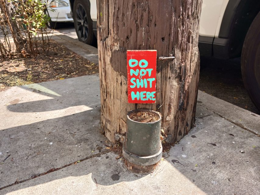 A wooden pole with a sign on it that says Do not shit here!