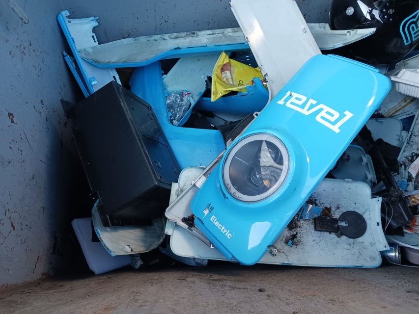 A disassembled e-scooter is sitting in a trash can.