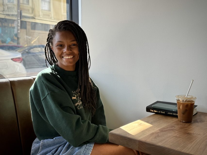 A young woman sitting at a table with a cup of coffee.