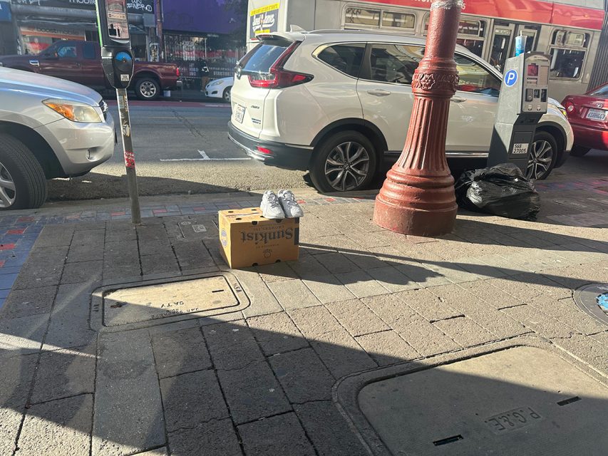 A box sitting on a sidewalk next to a car.