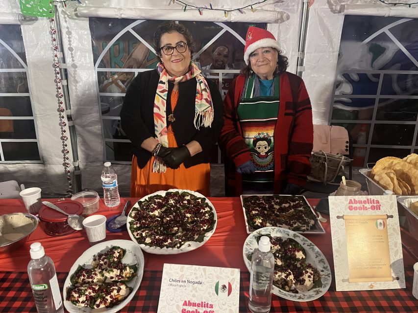 Two contestants in the abuelita cookoff standing in front of a table with their food on it.