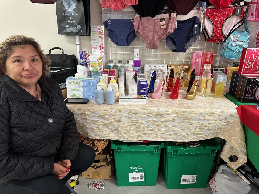 A woman sits in front of a table full of products.