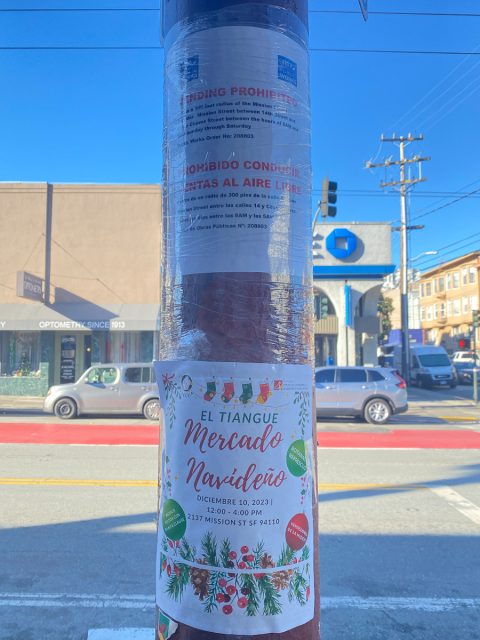 Two posters on a pole: the upper one is about prohibition on street-vending on Mission Street corridor, while the lower one is promoting El Tiangue, one of the two sanctioned indoor marketplaces on Mission Street.