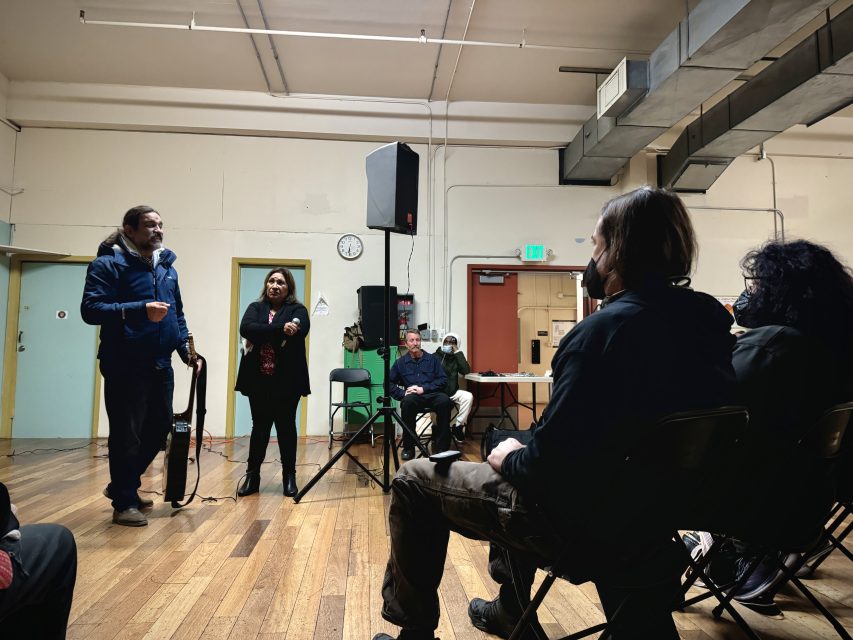 A man speaks to a group of people in a room.