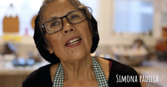 A woman wearing glasses and an apron in a kitchen.