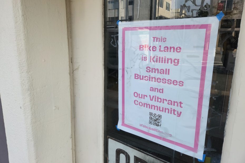 A sign on the door of a small business, reading “This Bike Lane is Killing Small Businesses and Our Vibrant Community.”