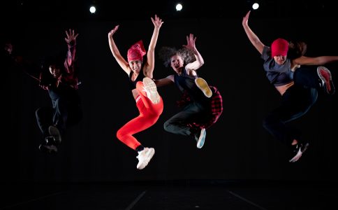 Four dancers jumping in the air on stage for a performance of Match Girrl