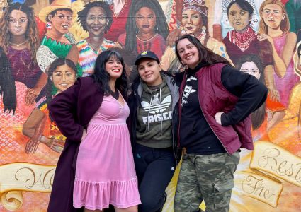 Three women posing in front of a mural of women at Balmy Alley and Lovers Lane.