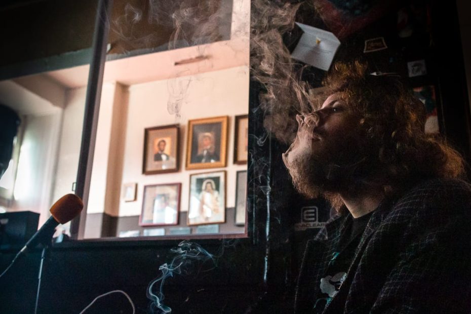 A man smoking a cigarette in front of a microphone.