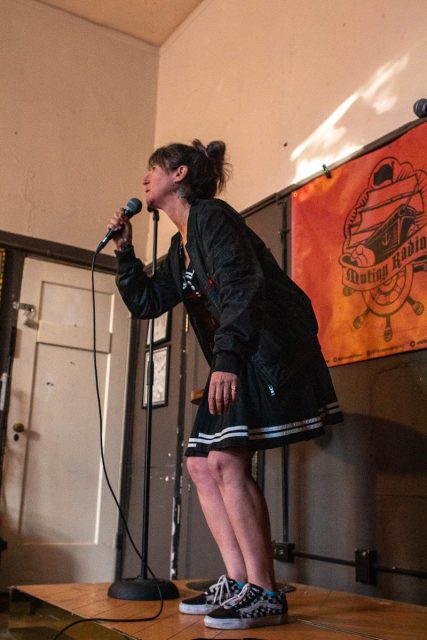 A woman in a black skirt singing into a microphone.