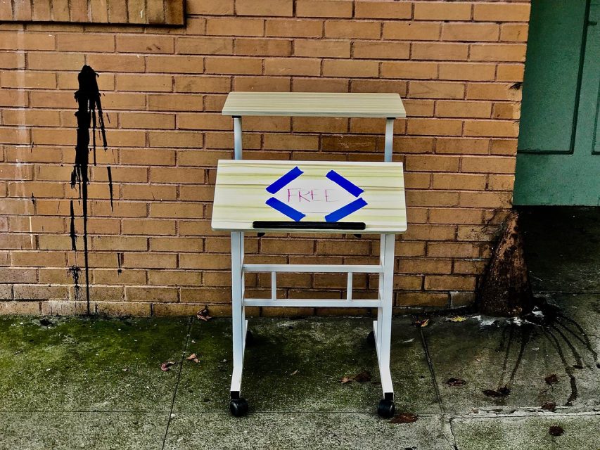 A small desk sitting on a sidewalk in front of a brick building.