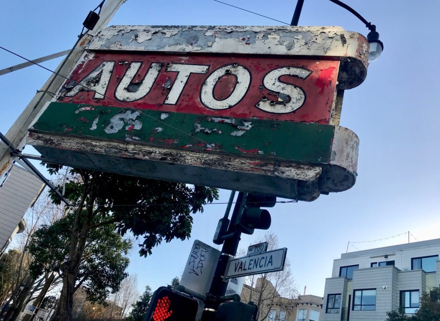 A rusty autos sign hangs on a street corner.